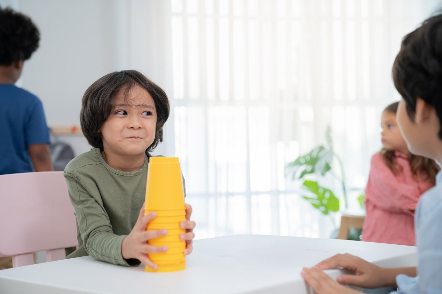A young boy participating in play-based behavioral therapy for kids in Singapore, focusing on fine motor skills and concentration by stacking yellow cups on a table.